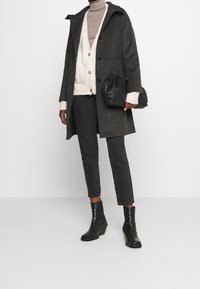 Szary wełniany płaszcz z kapturem, czarne guziki, zestawiony z kremowym swetrem z dzianiny, czarnymi dżinsami i botkami na kostkę. Czarna kopertówka dopełnia całość.