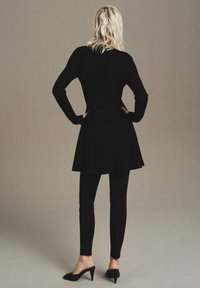 Black knit dress with flared hem, paired with black fitted leggings and pointed heels. Smooth texture, long sleeves, and minimalist design.