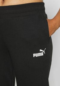Pantalones de chándal negros hechos de una tela suave, con un logo blanco de Puma en el lado izquierdo. Incluyen una cinturilla acanalada y bolsillos laterales.