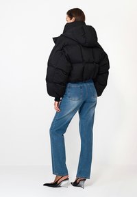 Czarna kurtka puchowa z kapturem, posiadająca pikowany wzór. W połączeniu z jasnoniebieskimi prostymi dżinsami i eleganckimi czarnymi butami na obcasie typu slingback.