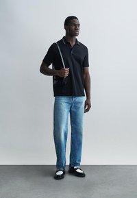 Čierne polo tričko s bielymi detailmi, svetlomodré rifle a čierno-biele topánky. Model drží malú čiernu kabelku na rameno.