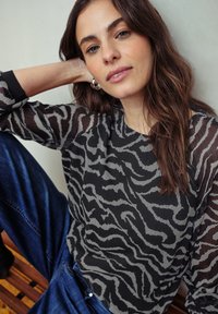 Top animalier in bianco e nero con maniche trasparenti, scollatura rotonda e vestibilità rilassata, abbinato a jeans in denim blu.