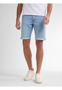 Shorts de mezclilla azul claro con dobladillos enrollados, combinados con zapatillas blancas. La tela tiene una textura suave y un ajuste relajado.