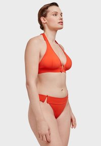 Rode bikini set met een haltertop met een diepe halslijn en een hooggewaist broekje. Soepele textuur en minimalistisch ontwerp met zijsplitten.