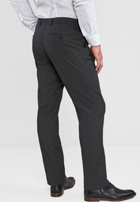Pantalones de vestir gris oscuro con una textura suave, ajuste entallado y detalle en el bolsillo trasero. Combinados con zapatos de cuero negros.
