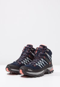Kesalahan hiking potongan menengah dengan bagian atas kain navy, aksen merah yang kontras, tali putih, sol karet yang bercorak, dan kotak jari yang diperkuat.