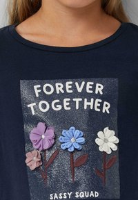 Marine t-shirt met een glinsterende grafiek met de tekst "VOOR ALTIJD SAMEN" en vier bloemenapplicaties in roze, paars, blauw en wit.