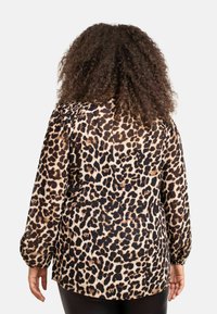 Blusa a stampa leopardata con maniche lunghe, vestibilità rilassata, motivo nero e tan, tessuto trasparente e scollatura rotonda. Accentuata da una morbida texture.