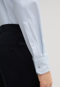 Lichtblauw patroon overhemd met een knoopmanchet, gecombineerd met donkere broek met een zwart logotag en knoopdetails.