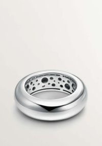 Anillo de plata con un exterior liso y redondeado y un interior hueco que presenta cortes circulares. Superficie reflectante con un acabado pulido.