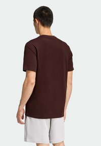 Hnedé bavlnené tričko s krátkymi rukávmi, okrúhlym výstrihom a voľným strihom, v kombinácii so svetlosivými textúrovanými kraťasmi.