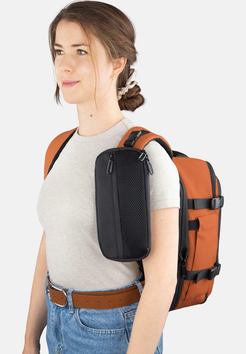 Oranger und schwarzer Rucksack mit gepolsterten Trägern, Reißverschlussfächern und einer strukturierten Vorderseite. Wird auf der Schulter einer Person in lässiger Kleidung getragen.