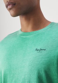 Groene katoen t-shirt met een ronde halslijn en een subtiele merklogo in het zwart op de borst, met een zachte, gestructureerde afwerking.
