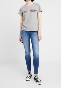 Šedé bavlněné tričko s textem "Good Times", vodorovné pruhy v růžové a modré barvě, v kombinaci s modrými skinny jeans a černými teniskami.