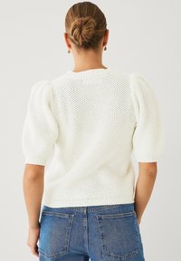 Maglione bianco lavorato a maglia con maniche a sbuffo e polsini a costine, caratterizzato da un motivo testurizzato. Abbinato a jeans in denim blu. Mostrata vista posteriore.