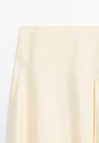 Roomkleurige satijnen roksectie met diagonale naaddetail en een gladde, vloeiende stoftextuur.