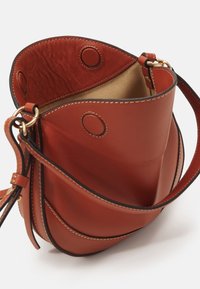 Leren emmer tas in diep oranje met een soepele textuur, ronde accenten en een contrasterende zwarte randstiksels. Inclusief een verstelbare schouderriem.