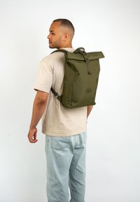 Zöld, felhajtható hátizsák tartós anyagból, egycsatos zárással, oldalsó zsebbel és minimalista kialakítással.