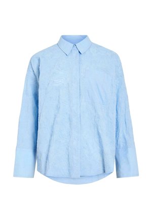 Camisa azul claro de manga larga con sutil patrón floral en relieve, cuello puntiagudo, bolsillo delantero y puños abotonados.