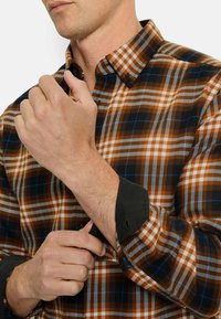 Braun, blau und weiß kariertes Button-Up-Hemd mit schwarzen Manschetten, das einen Kentkragen und kontrastierende Manschettendetails aufweist.