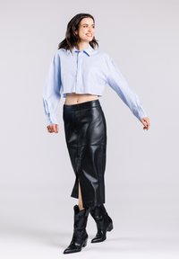 Korte lichtblauwe shirt met een voorkeurszak, gecombineerd met een zwarte leren rok met een zijsplit, en zwarte cowboylaarzen met decoratieve accenten.