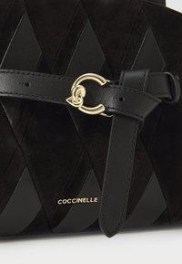 Borsa in suede nera con motivo a rombi trapuntato, dotata di una tracolla in pelle nera e di una chiusura circolare dorata. Logo "Coccinelle" in oro.