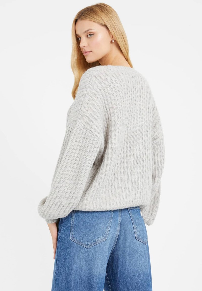 Hellgrauer, lockerer Strickpullover mit ribbeliger Textur und überschnittenen Schultern, kombiniert mit hochgeschnittenen blauen Jeans.