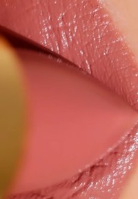 Matt rosa Lippenstift mit einer glatten Textur und leichtem Glanz, der detaillierte Oberflächenlinien und Konturen vor einem verschwommenen Hintergrund zeigt.