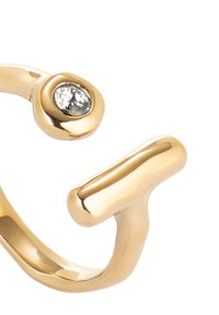 Bague en métal doré avec un design lisse et courbé, ornée d'une pierre ovale transparente et d'une finition polie, mettant en avant une esthétique moderne et minimaliste.