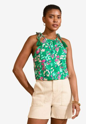Top senza maniche verde con una stampa leopardata colorata, dotato di spalline legate e nappine; abbinato a pantaloni corti beige chiaro.