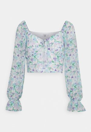 Blouse courte à manches longues en tissu transparent avec un motif floral dans des tons de vert et de violet. Présente un décolleté carré et un détail à nouer.