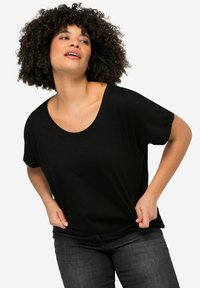 Černé tričko s krátkým rukávem, širokým kulatým výstřihem a volným střihem. Modelka ho nosí s tmavými džíny, přičemž je vidět jemná textura látky.