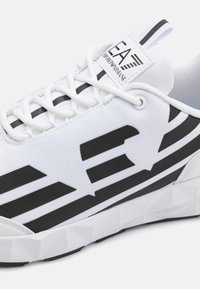 Hvide sneakers med en struktureret tekstiloverdel med fede sorte striber, runde snørebånd og en geometrisk hvid gummisål.