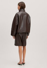 Bruine leren oversized jas met een hoge kraag, gecombineerd met een bijpassende leren rok tot de knie. Glad oppervlak, minimale details.