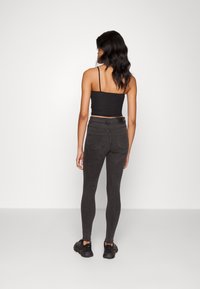 Top curto preto e jeans pretos justos com uma textura suave. Ajuste skinny com bolsos traseiros e detalhes de hardware mínimos.