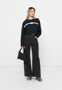 Haut noir court à manches longues avec une rayure blanche, jean évasé noir taille haute, et un sac à main noir avec une texture lisse et un design courbé.