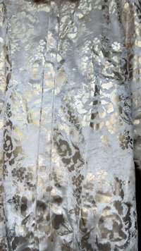 Silkete sølvfarge stoff med et blomsterdesign i gull og mørkebrunt. Teksturen er glatt, med reflekterende aksenter som fremhever designet.