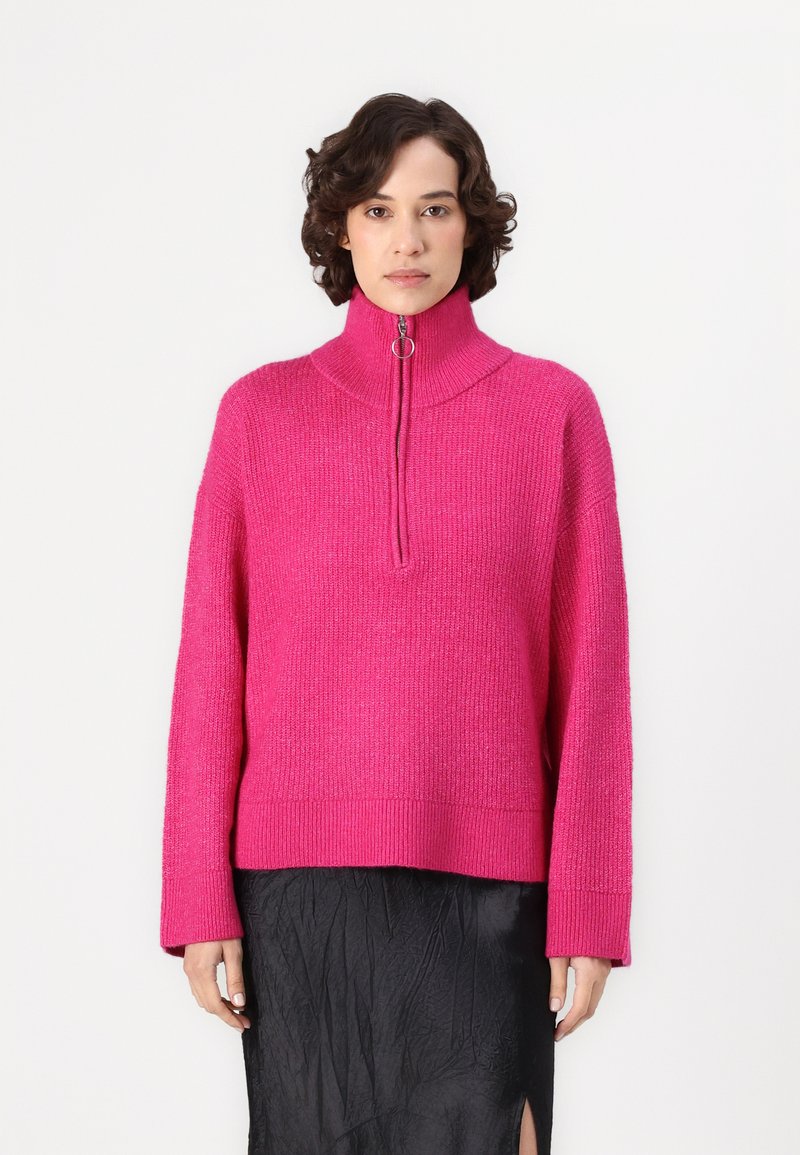 Fuksjowy różowy sweter z dzianiny z wysokim kołnierzem i ćwierć-zamkiem. Posiada szerokie rękawy i luźny krój.