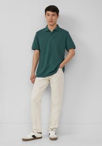 Teal Poloshirt mit lässiger Passform und kurzen Ärmeln, kombiniert mit cremefarbenen Hosen und weißen Sneakers mit schwarzen Akzenten.