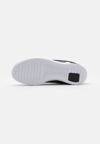 Black shoe sole with a textured surface, featuring a white rubber outsole and horizontal grooves for traction. Black accent logo present.