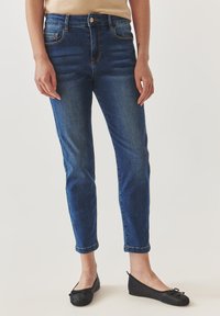 Jeans de mezclilla azul oscuro con corte slim, cintura media y puños enrollados. Presentan un estilo clásico de cinco bolsillos y un cierre de botón de cobre.