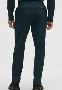 Dunkelgrüne Sporthose mit schmal zulaufender Passform, elastischem Bund und seitlichen Taschen. Das Material wirkt glatt mit mattem Finish.