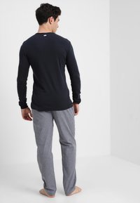 Chemise à manches longues bleu marine avec col rond, associée à un pantalon de pyjama à carreaux gris et blancs, offrant une coupe décontractée et un tissu léger.