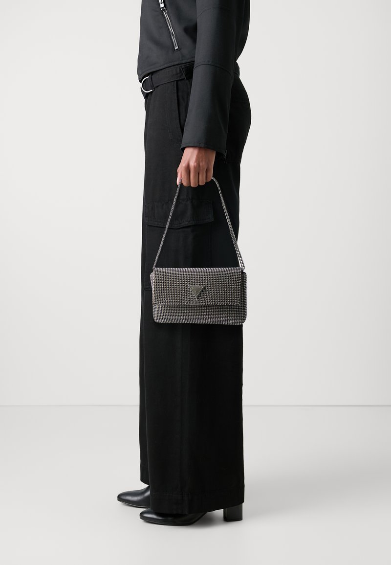 Sac à main gris métallique avec un design tressé, doté d'un rabat à pli et d'une anse en chaîne argentée. Porté avec un pantalon large noir et des talons.
