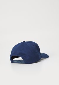 Gorra azul marino hecha de una mezcla de algodón, con visera curva, cierre ajustable a presión y ojales ventilados para la transpirabilidad.