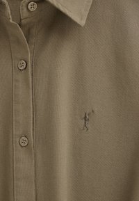 Gros plan sur un polo vert olive avec des boutons et un petit golfeur brodé tenant un club sur la poitrine.