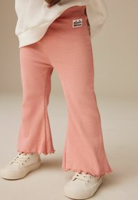 Rosa ribbade utsvängda byxor med scallopkant och ett "Minnie Mouse" logotyp-patch; tillsammans med vita sneakers. Mjuk textur, åtsittande design.