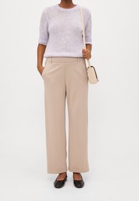 Světle fialový pletený svetr s krátkým rukávem; béžové široké kalhoty s bočními kapsami; černé baleríny; malá béžová kabelka.