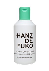 Vit flaska med ett mintgrönt flip-top lock. Svart text med orden "HANZ DE FUKO NATURAL CONDITIONER." Innehåller detaljer om ingredienser och tillsatser.