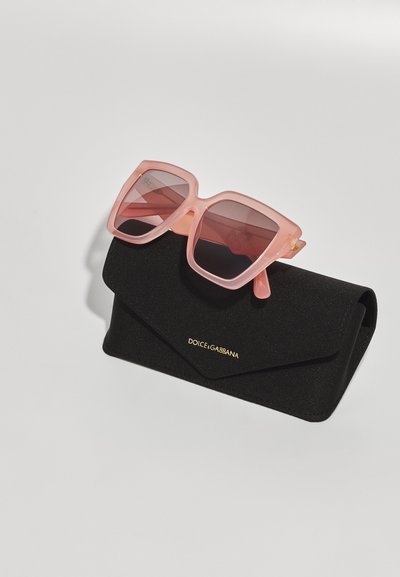 Ružičaste oversize sunčane naočale s gradijentnim staklima odmaraju se na crnoj teksturiranoj futroli, s zlatnim natpisom "DOLCE & GABBANA".